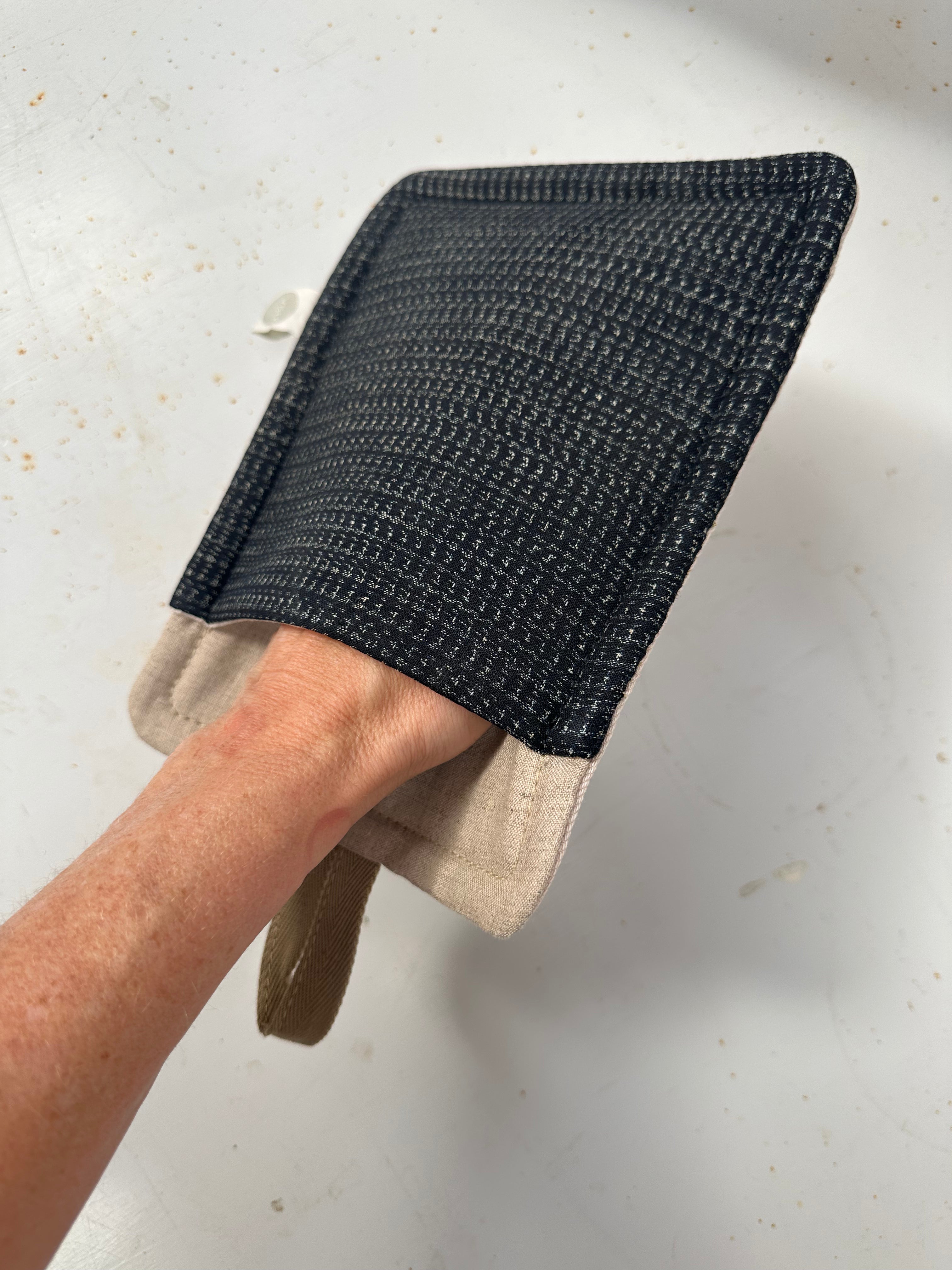 Hand wearing a black textured oven mitt on a light background